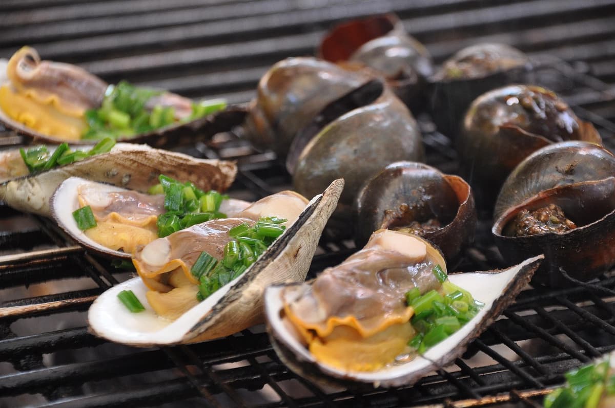 A street food stall in Can Tho displays steaming pots of soup, a tray of fresh herbs, and stacks of folded plate-sized banh xeo crepes