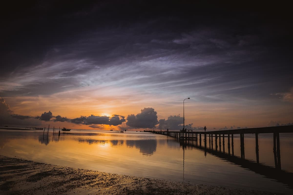 A long crescent of pale sand on Long Beach in Phu Quoc with wooden loungers in the foreground and a sunset turning the water gold