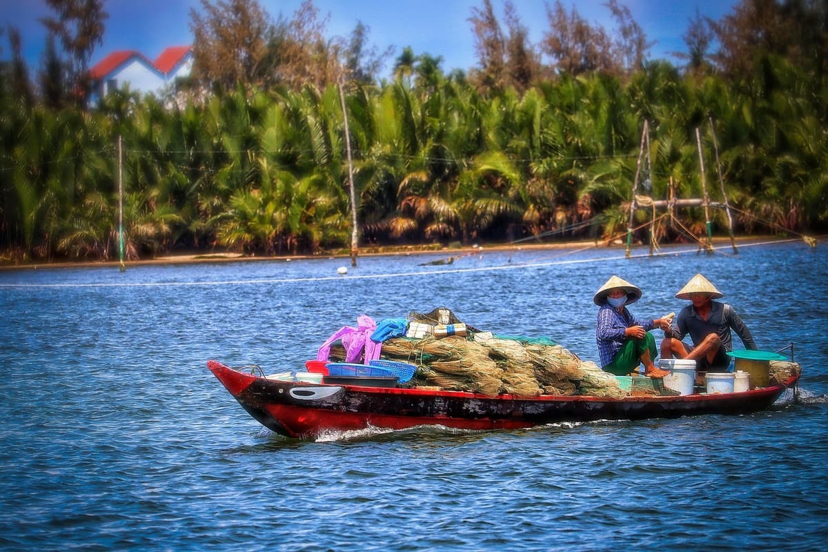 A wide curve of the Hau River in Can Tho reflects palm trees and a small wooden cargo boat under a soft morning sky